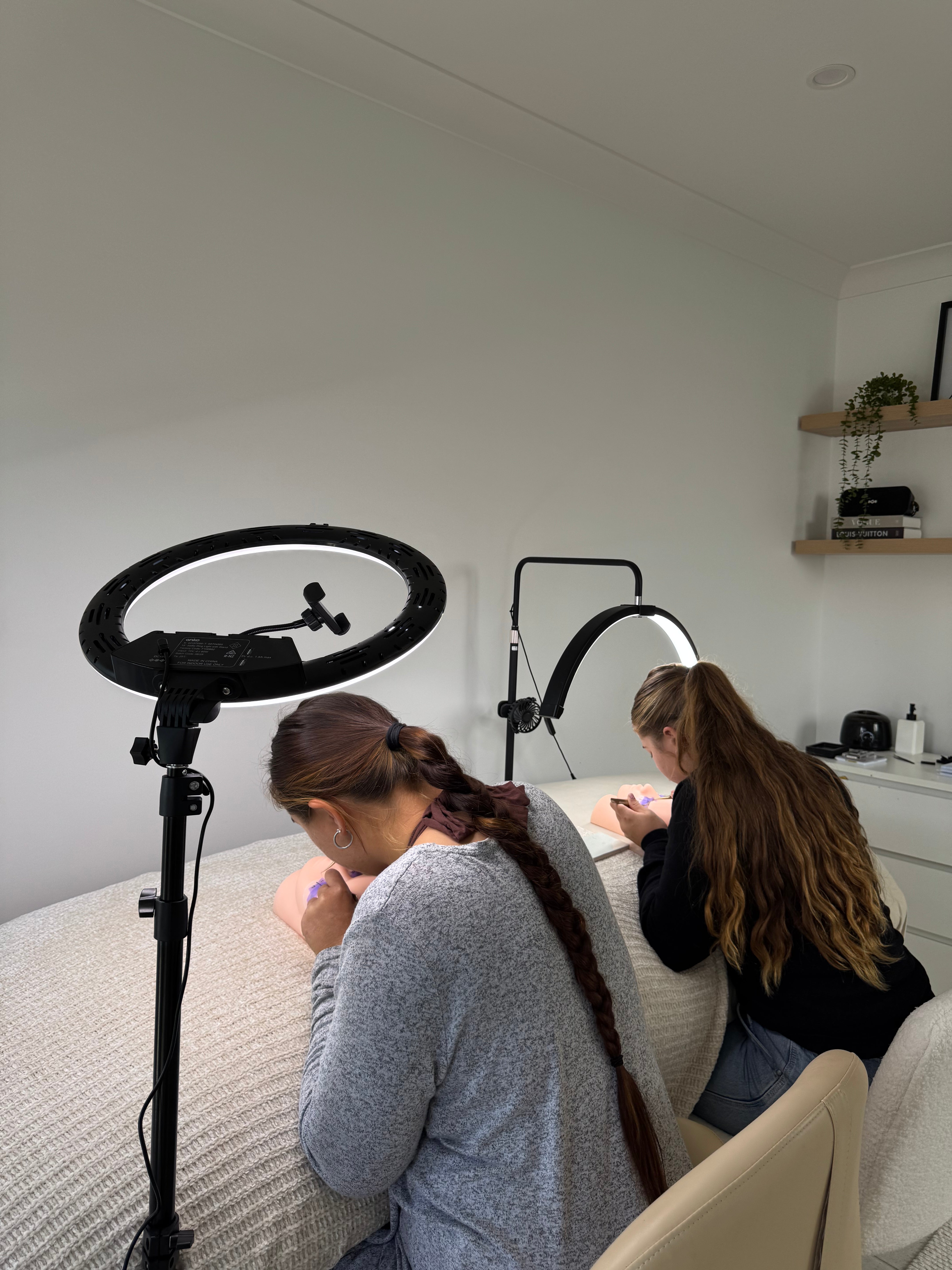 Two LBHR students practising lash application side by side under ring lights in the Burpengary studio
